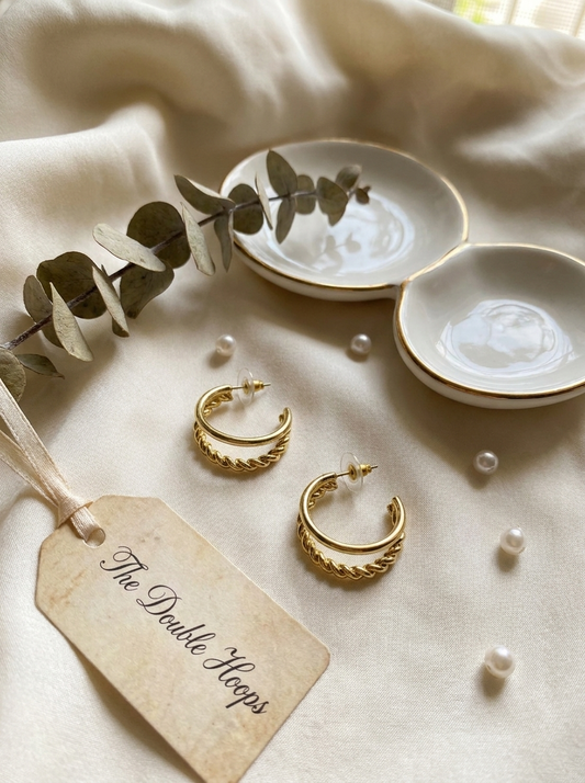 The Double Hoops gold earrings on travertine stone with dried flowers and pink silk