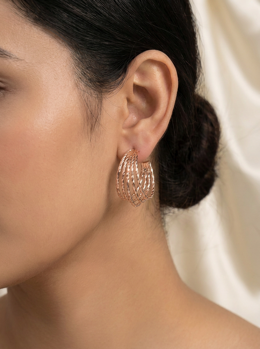 Close-up of model wearing rose gold multi-strand twisted hoop earrings with cream silk background