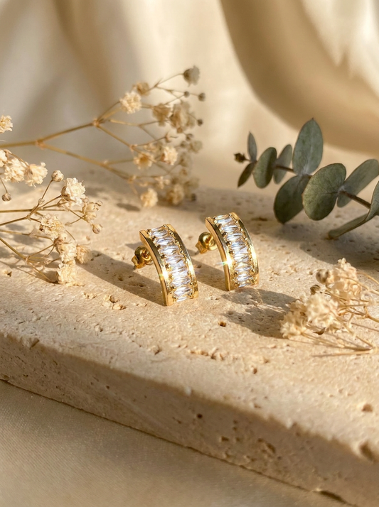 Baguette crystal hoop earrings flatlay on cream silk with gold rings and rose quartz crystal