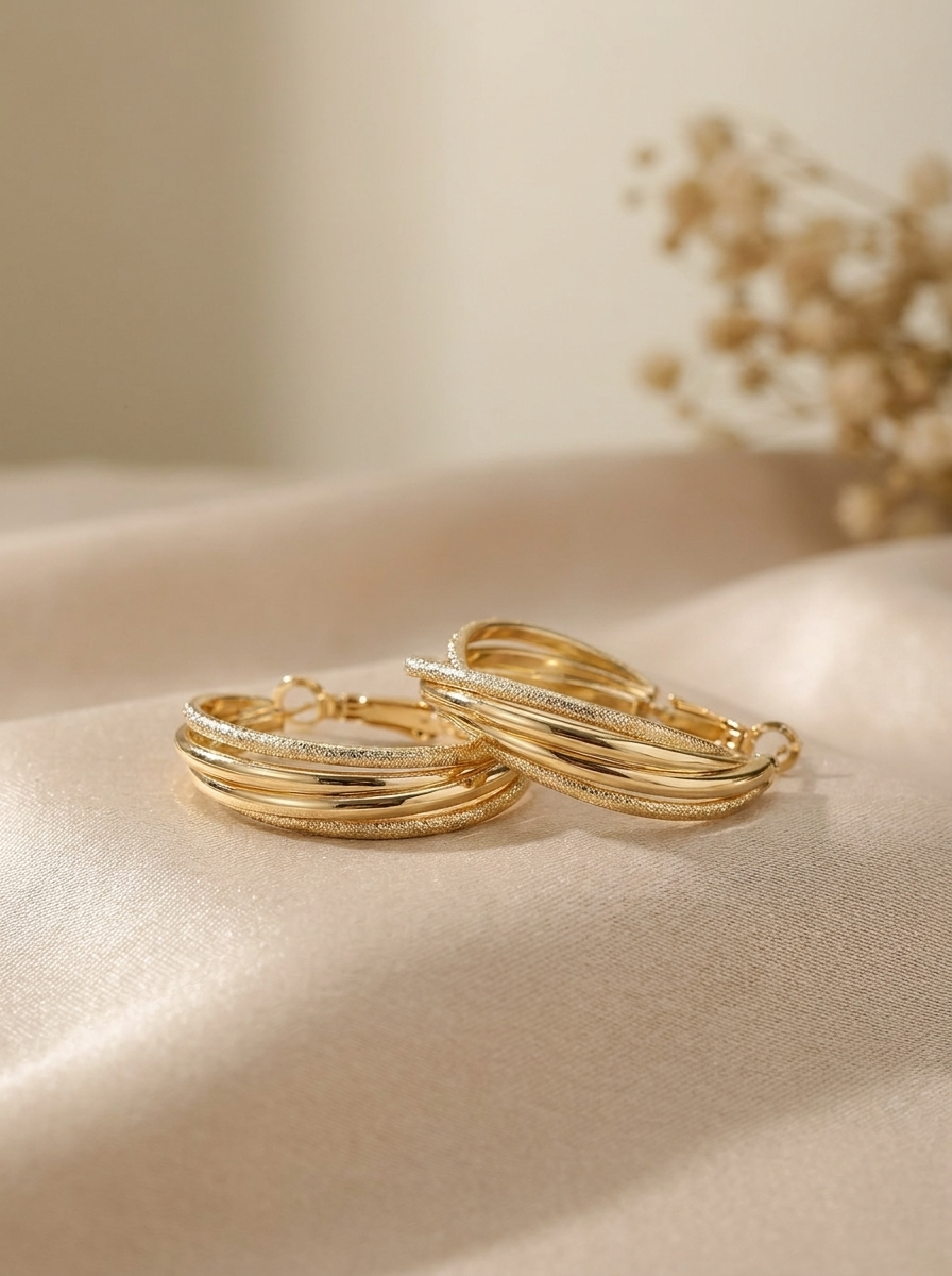 The Twisted Trio Hoops gold multi-strand hoop earrings on cream silk with dried flowers
