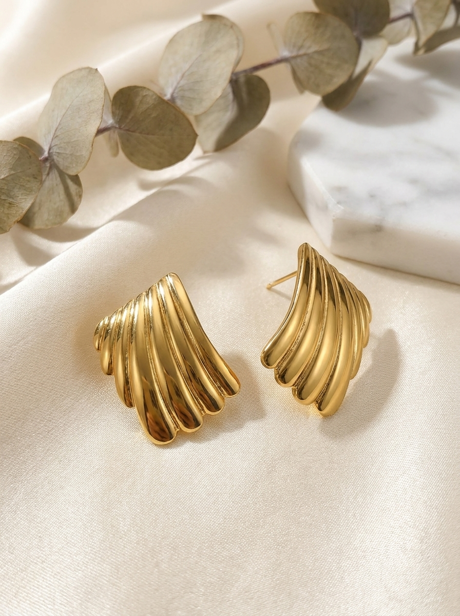 The Shell Studs gold sculptural stud earrings on cream silk with eucalyptus and marble
