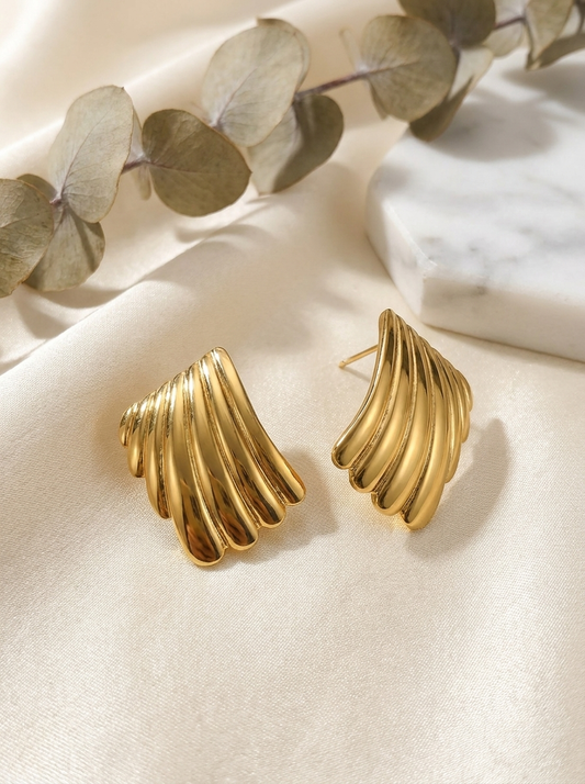 The Shell Studs gold sculptural stud earrings on cream silk with eucalyptus and marble