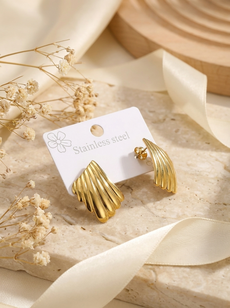 The Shell Studs gold stud earrings on packaging card with ribbon and dried flowers on stone