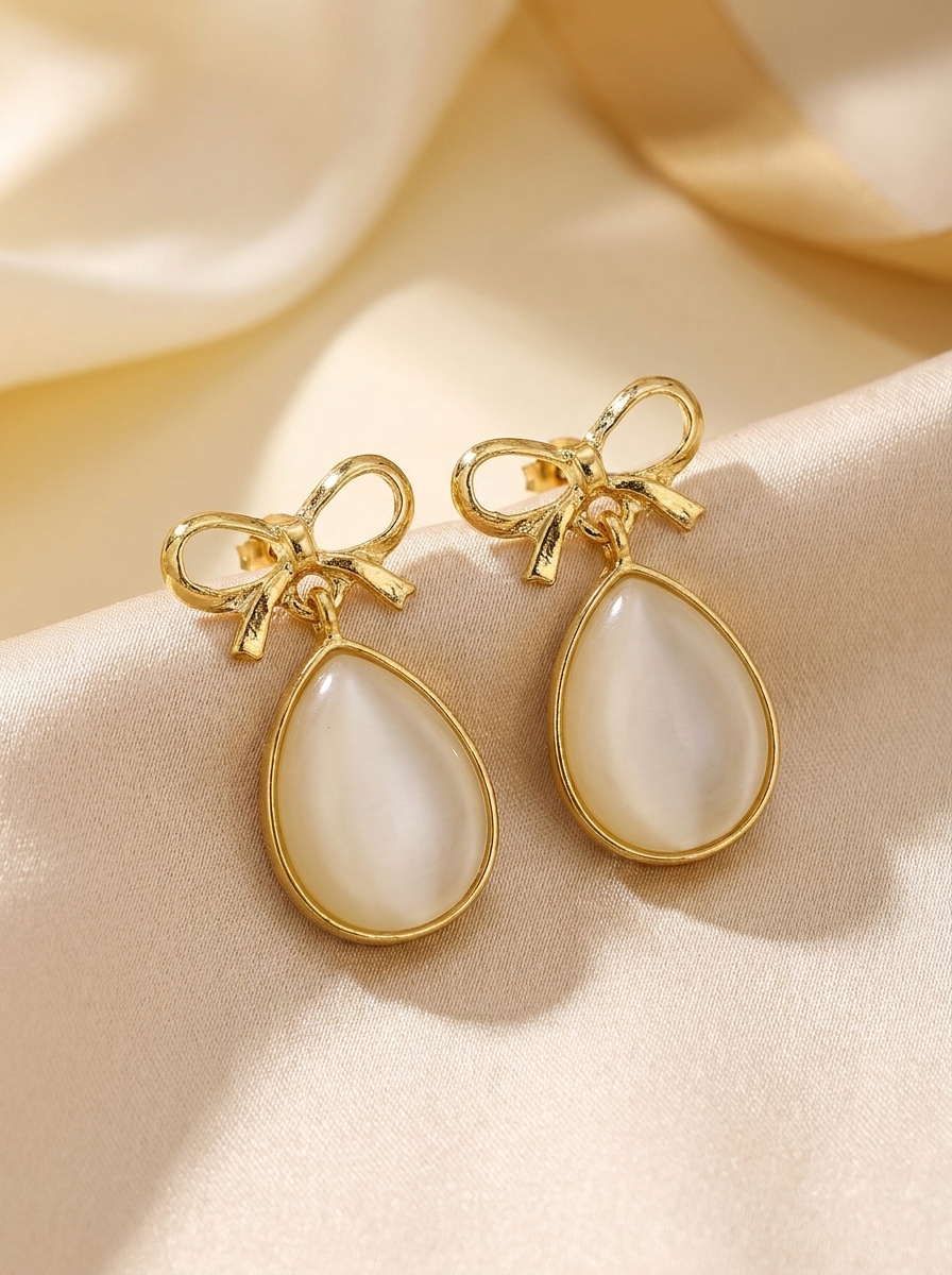 Bow and pearl drop earrings close-up on gold silk showing bow detail and mother of pearl teardrop