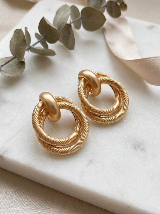 Matte gold twisted knot earrings on marble with eucalyptus leaves