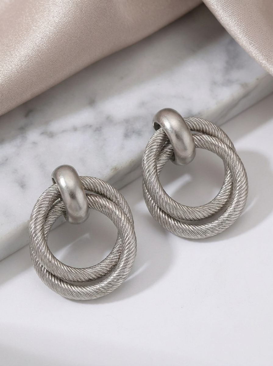 Silver twisted double hoop earrings on marble surface with cream satin fabric